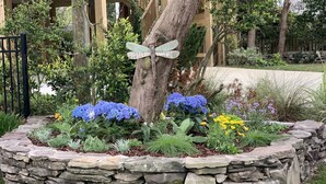 A garden with a stone border, blue hydrangeas, and a butterfly sculpture.