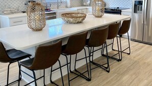 A modern kitchen with white cabinets, stainless steel appliances, a large island with bar stools, and decorative woven baskets.
