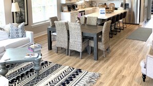 A modern kitchen with a central island, a dining area with wicker chairs, and a ceiling fan.