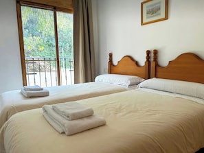 A hotel room with two beds, a balcony with a view, and a framed picture on the wall.