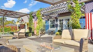 An outdoor patio area with wicker furniture, a glass-top table with a fire feature, and American flags.