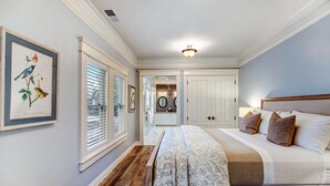 A bedroom with a large bed, a nightstand, a dresser, and a window with blinds.