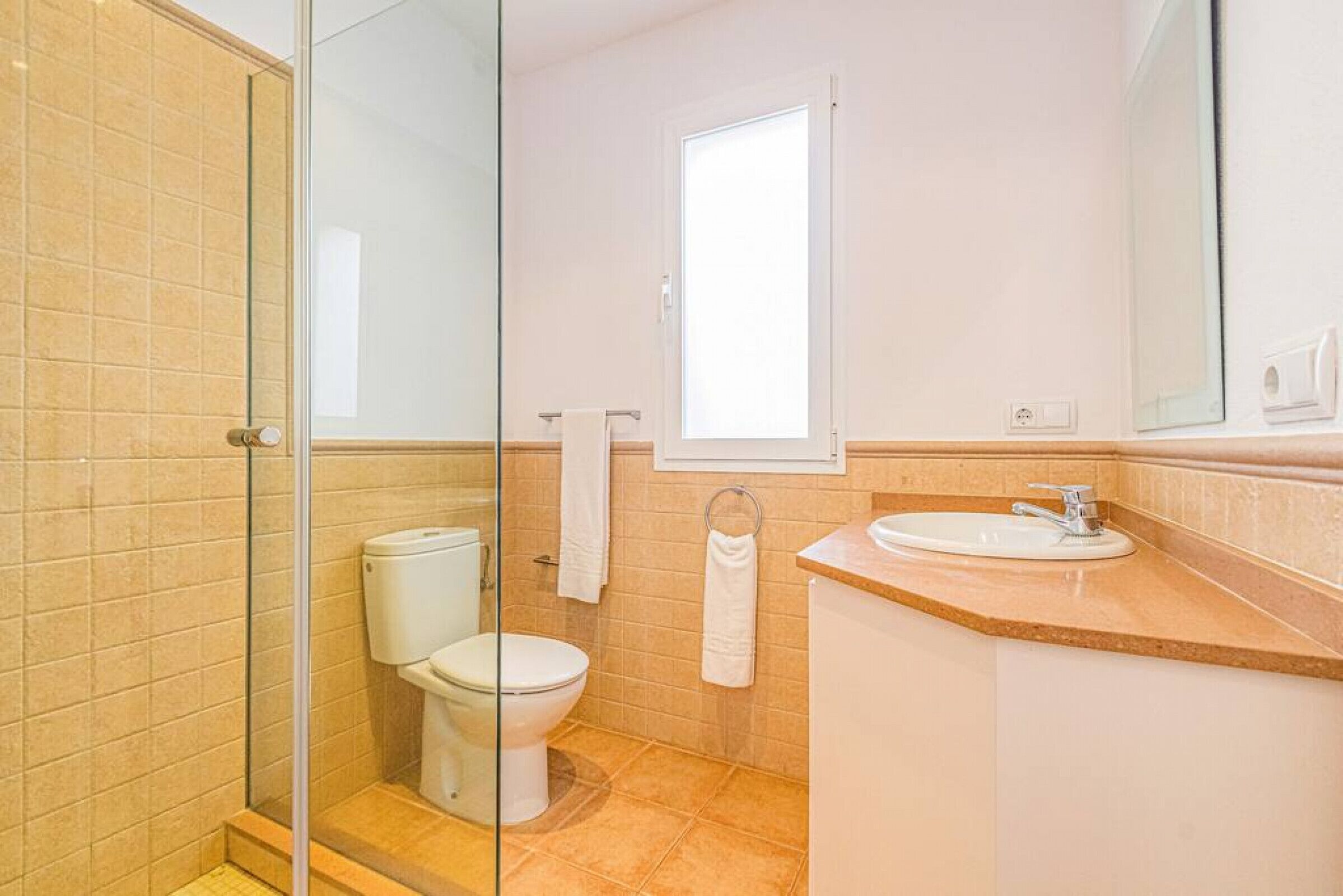 A bathroom with a glass shower enclosure, a toilet, a sink, and a window.