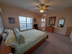 A bedroom with a bed, a ceiling fan, a dresser, a mirror, and a window with blinds.