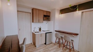 A compact kitchen with wooden cabinets, a microwave, a sink, and a small dining area with a wooden table and two chairs. - Cozy Retreat with Breathtaking Views, 20 Minutes to the Airport (Alajuela)