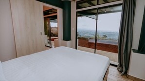 A bedroom with a large bed, a sliding glass door leading to an outdoor area, and a view of the landscape. - Cozy Retreat with Breathtaking Views, 20 Minutes to the Airport (Alajuela)