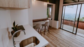 A modern kitchen with a stainless steel sink, bar stools, and a view through large sliding glass doors. - Cozy Retreat with Breathtaking Views, 20 Minutes to the Airport (Alajuela)