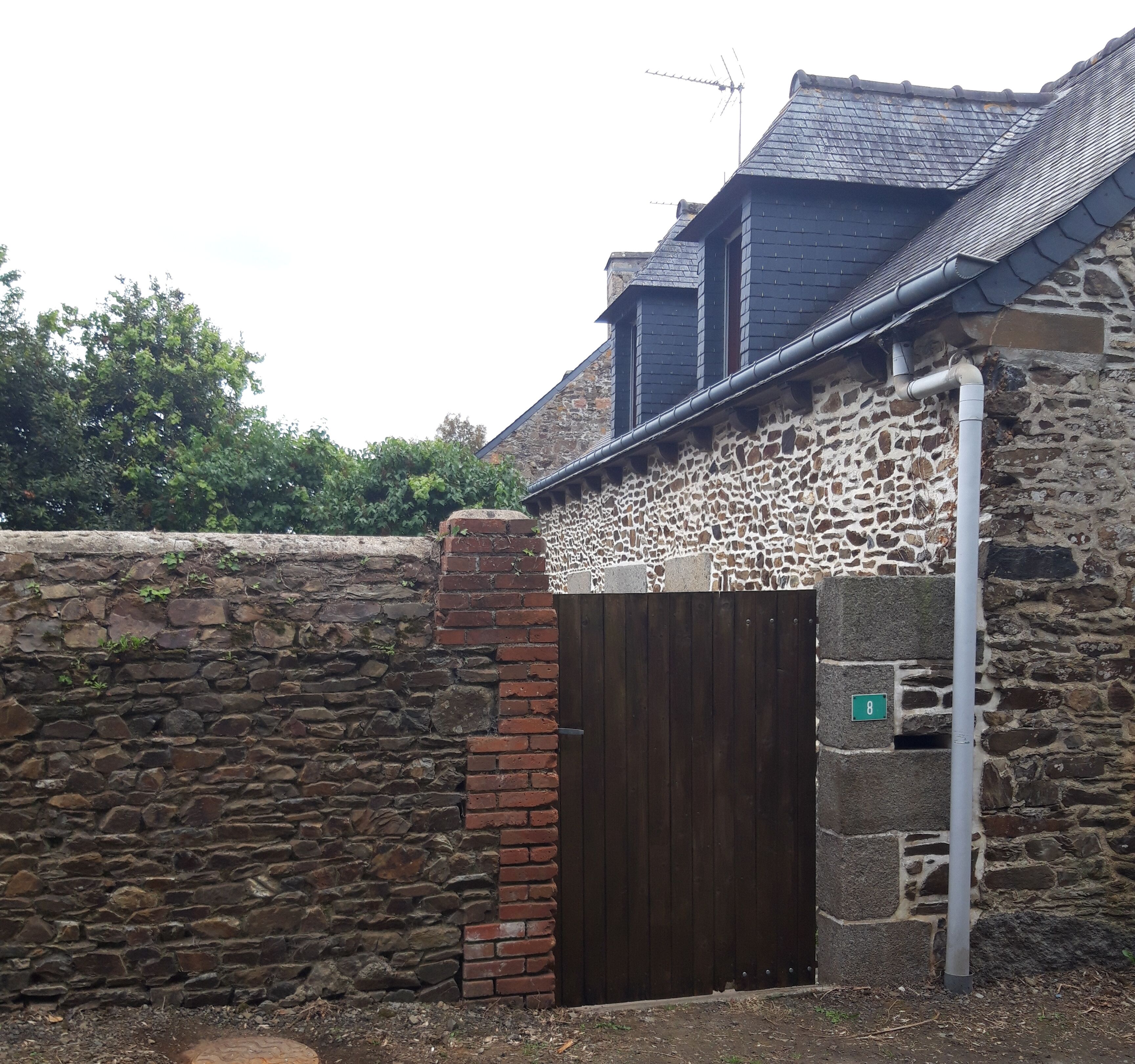 A stone wall with a wooden gate, a brick chimney, and a metal pipe.