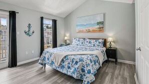 Un dormitorio con cama, dos mesitas de noche, ventilador de techo, un cuadro y vistas al exterior.