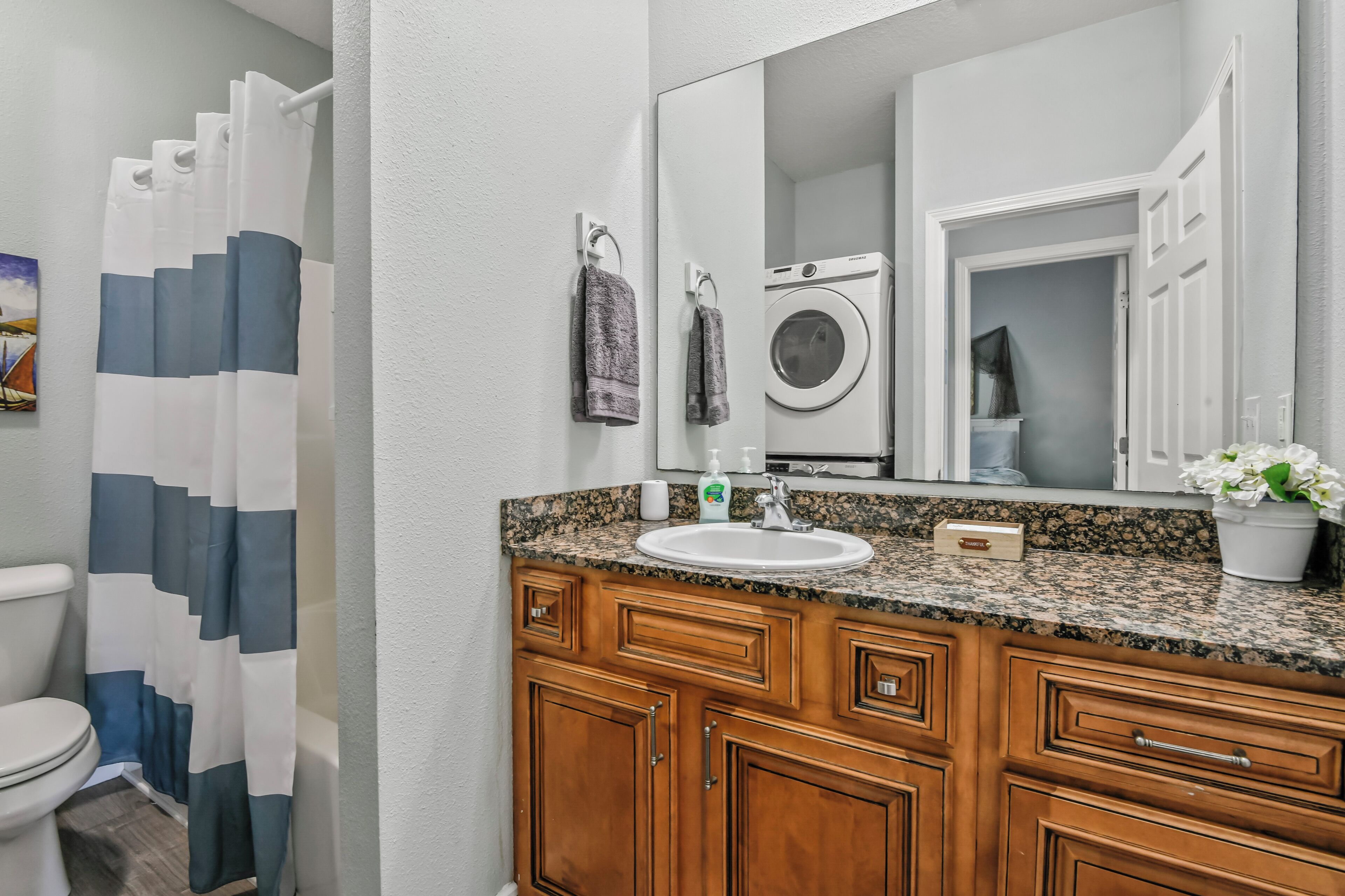 A bathroom with a white toilet, a shower curtain, a sink with a soap dispenser, a mirror, and wooden cabinets.