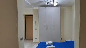 Ein Hotelzimmer mit Kleiderschrank, einem Bett mit blauer Bettdecke, einem Nachttisch mit Fernbedienung und einer Deckenleuchte.