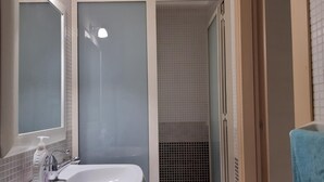 Ein Badezimmer mit einem weißen Waschbecken, einem Spiegel und einer Duschkabine mit gefliesten Wänden.