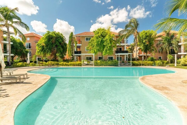 A resort pool with clear water, surrounded by palm trees and a building with balconies.