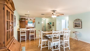 A spacious dining area with a wooden table and white chairs, a ceiling fan, and a view into the kitchen. - 🍹🌞 Cottage Paradise! 2BR/2BA, Pets Welcome, TV, Wi-Fi (Sebastian)