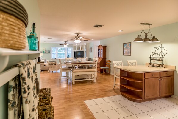A spacious kitchen with wooden cabinets, a dining area with white chairs, and a ceiling fan.