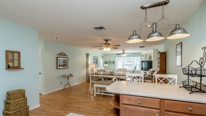 A spacious kitchen with wooden cabinets, a dining area with white furniture, and a ceiling fan. - 🍹🌞 Cottage Paradise! 2BR/2BA, Pets Welcome, TV, Wi-Fi (Sebastian)