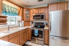 A modern kitchen with wooden cabinets, stainless steel appliances, and a large window with a view. - 🍹🌞 Cottage Paradise! 2BR/2BA, Pets Welcome, TV, Wi-Fi (Sebastian)
