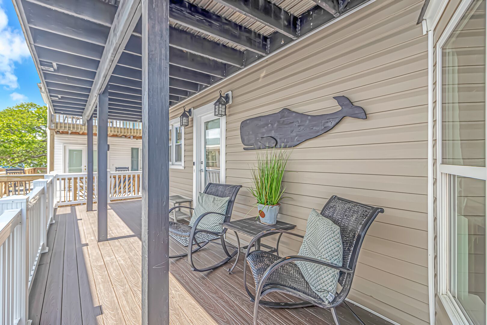A covered outdoor area with a wooden deck, two wicker chairs, a table, and a potted plant.