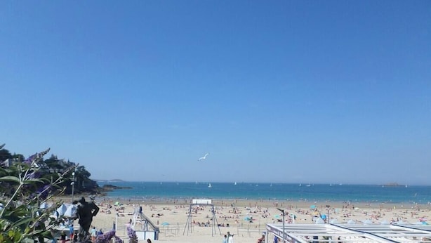 Una playa con una estatua, sombrillas de playa y un letrero que dice 'Brasserie Le Bar du Soleil'.