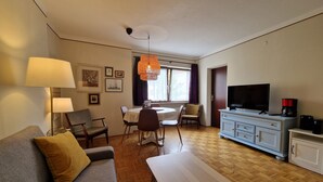 A living room with a sofa, a dining table with chairs, a TV, and a coffee maker. - Apartment Centrum für 4 Personen (Zell am See)