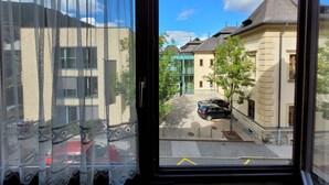 A view from a window with lace curtains, looking out onto a street with parked cars and buildings. - Apartment Centrum für 4 Personen (Zell am See)