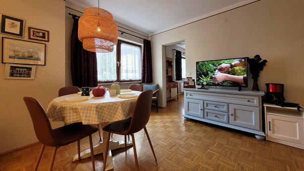 A dining area with a table set for two, a television on a cabinet, and framed pictures on the wall. - Apartment Centrum für 4 Personen (Zell am See)