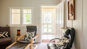 A room with a brown sofa, a wooden rocking chair with floral cushions, a black leather chair with floral cushions, and a door leading outside.