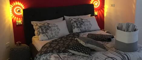 A bedroom with a bed, pillows, a throw blanket, a side table, and wall-mounted lights.