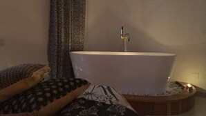 Un baño con una bañera independiente, cortinas estampadas y una pequeña bandeja de madera redonda para el baño.