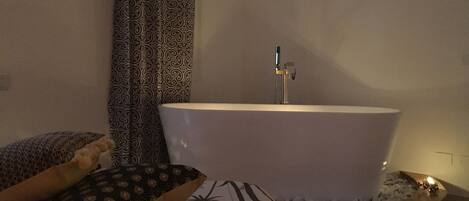 A bathroom with a freestanding bathtub, patterned curtains, and a small, round, wooden bath tray.