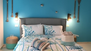Un dormitorio con pared azul, cabecera gris y cama con colcha a rayas. Hay dos luces fijadas a la pared y varias palas de madera en la pared.