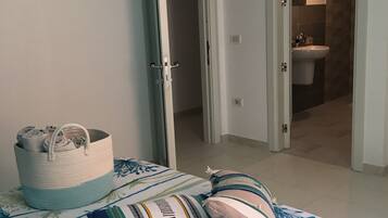 Camera da letto con un letto, un cesto portaoggetti e un bagno visibile attraverso una porta aperta.
