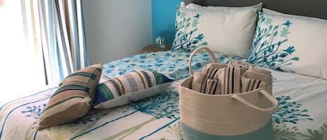 A bedroom with a bed, pillows, a woven basket, and wall-mounted items.