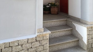 Una entrada de edificio con puerta roja, ventana con rejas decorativas y un cartel en la pared.