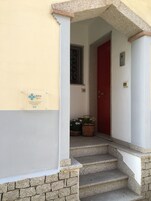 Une entrée d’immeuble avec une porte rouge, une fenêtre ornée de barreaux en fer et une enseigne sur le mur.