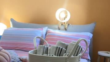 Un lit avec une literie à rayures, une lampe de chevet, un panier en osier et un miroir fixé au mur.