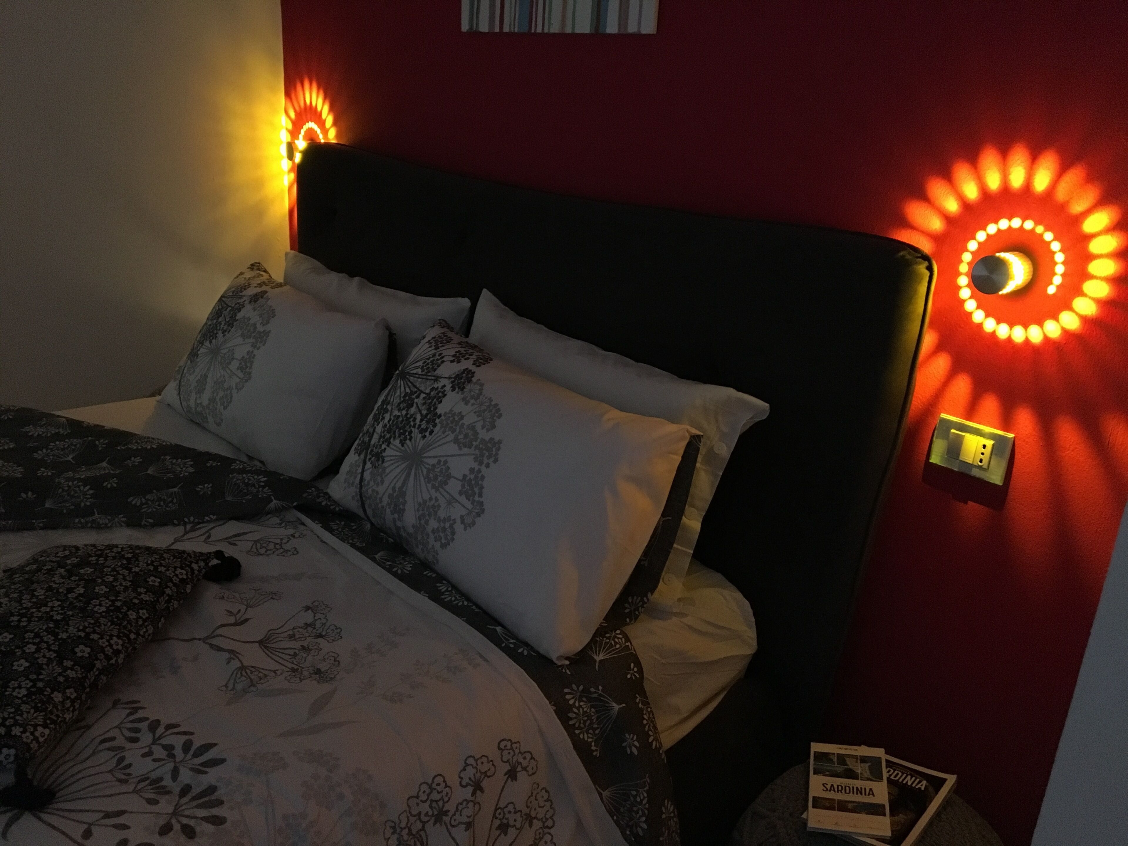 Una cama con ropa de cama de estampado floral, un cabecero oscuro y dos lámparas de pared con diseños circulares.