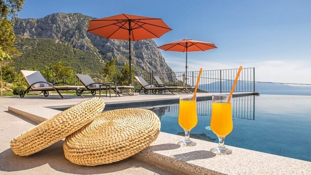 Zona de piscina amb gandules, dues ombrel·les i dos gots de suc d'aranja.