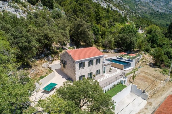 A two-story stone house with a red-tiled roof, a swimming pool, and a small garden.