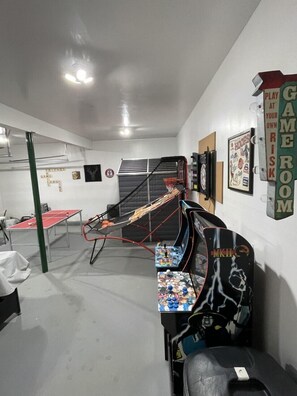 Una habitación con mesa de ping pong, aro de baloncesto, consola de videojuegos y un cartel en la pared.