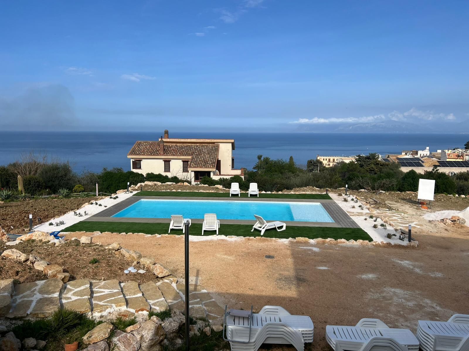 Una piscina con sillas de descanso, una casa y vista al mar.