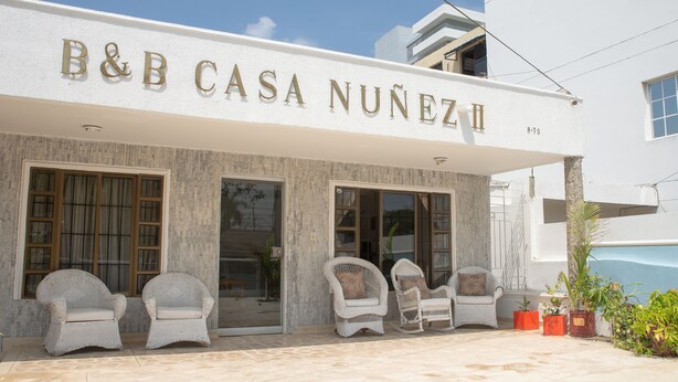 Un hôtel appelé B&B CASA NUÑEZ, avec une façade blanche, de grandes fenêtres et des chaises en osier à l’extérieur.