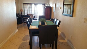 A dining area with a rectangular table, multiple chairs, a potted plant, and a lamp. - Dawn 1024 (Galveston)