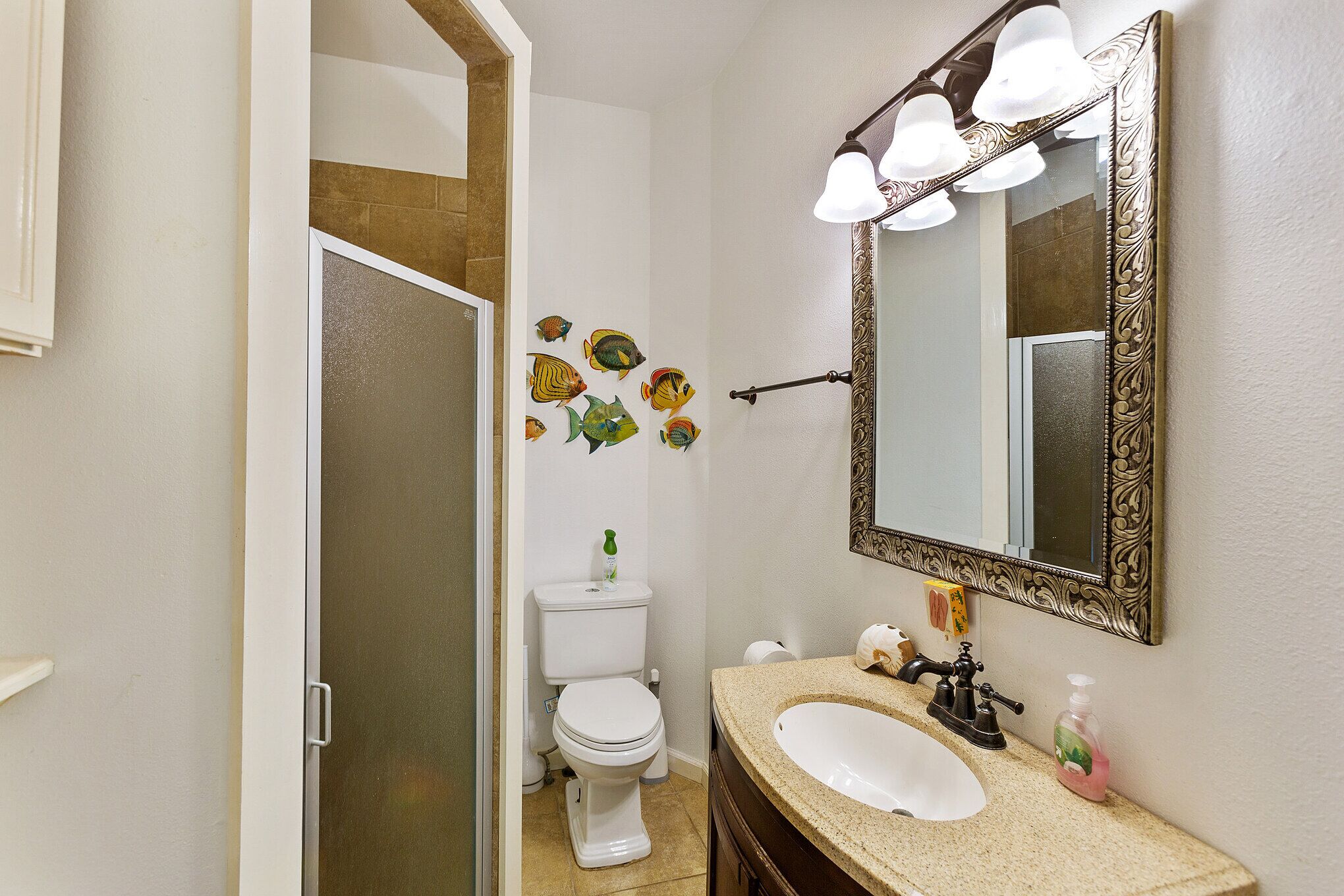 A bathroom with a white toilet, a beige sink, and a mirror with a decorative frame.