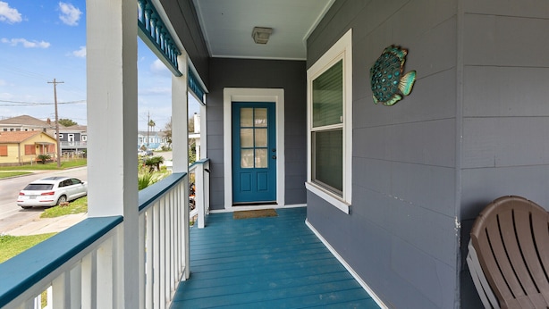 A porch with a blue railing, a blue door, and a brown chair. - Tina Marie (Galveston)