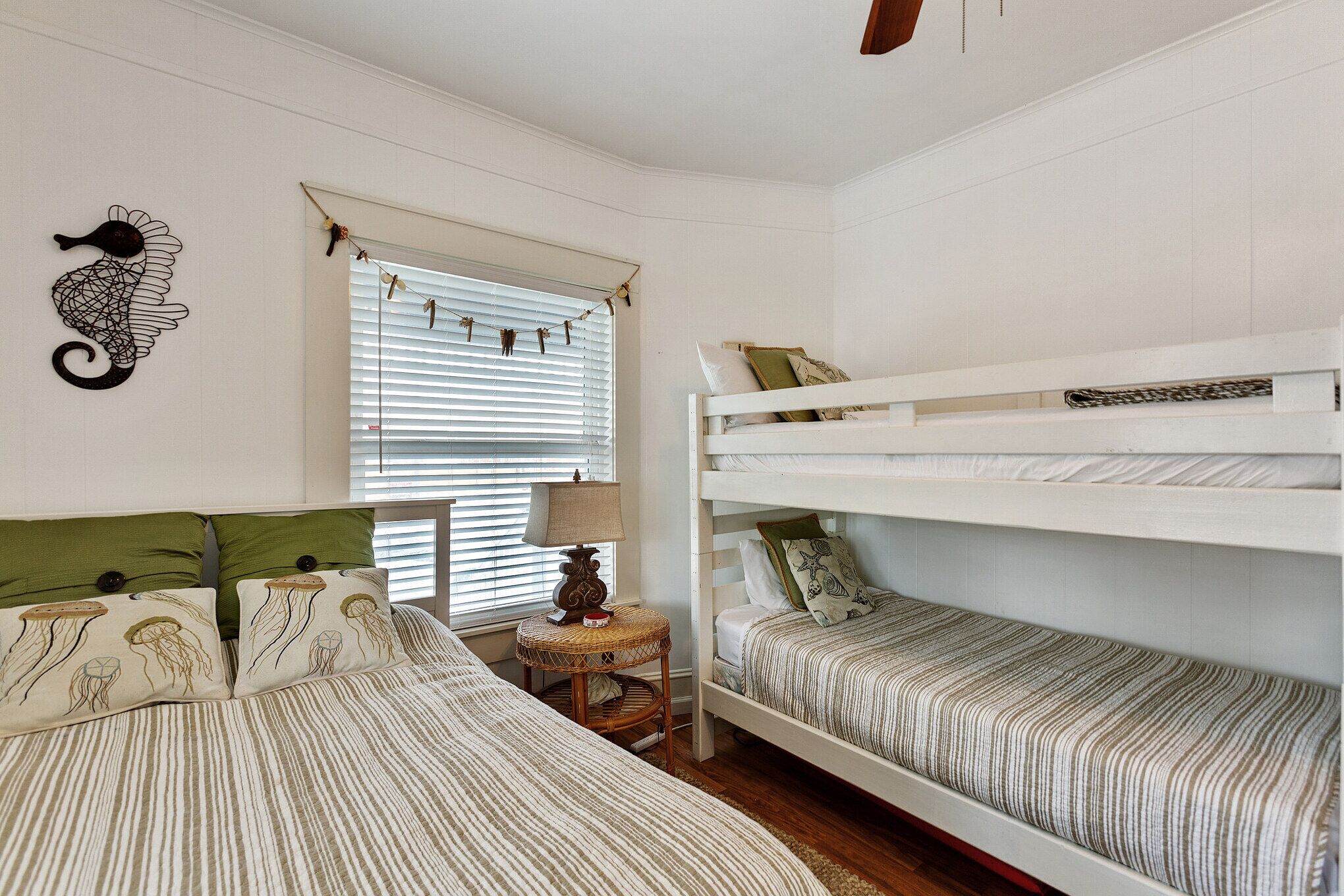 A bedroom with two bunk beds, a bedside table with a lamp, and a decorative seahorse wall art.