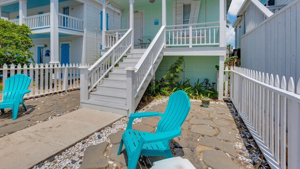 Un edificio de dos pisos con un porche, barandillas blancas y una escalera que conduce al piso superior.