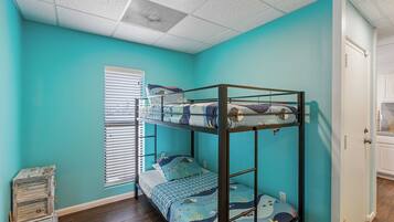 A bunk bed room with teal walls, a wooden floor, and a window with blinds.