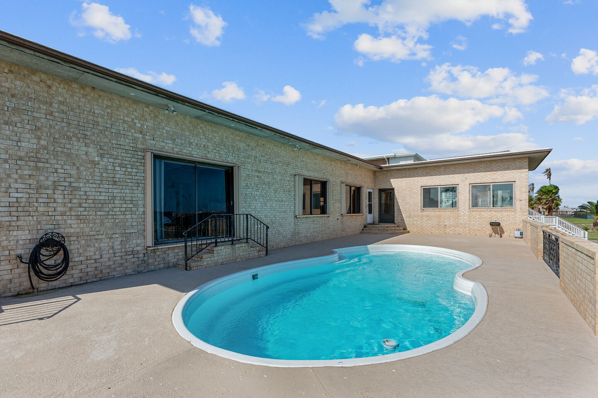 A swimming pool area with a brick building, a covered patio, and a clear blue sky.