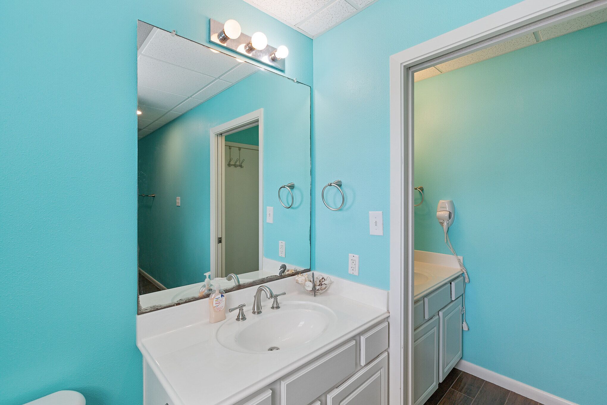 Een badkamer met turquoise wanden, een witte wastafel en een grote spiegel met verlichting erboven.